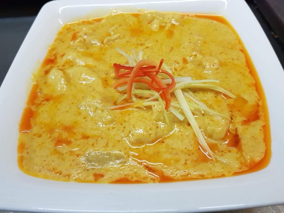 A white plate topped with a yellow curry and vegetables.