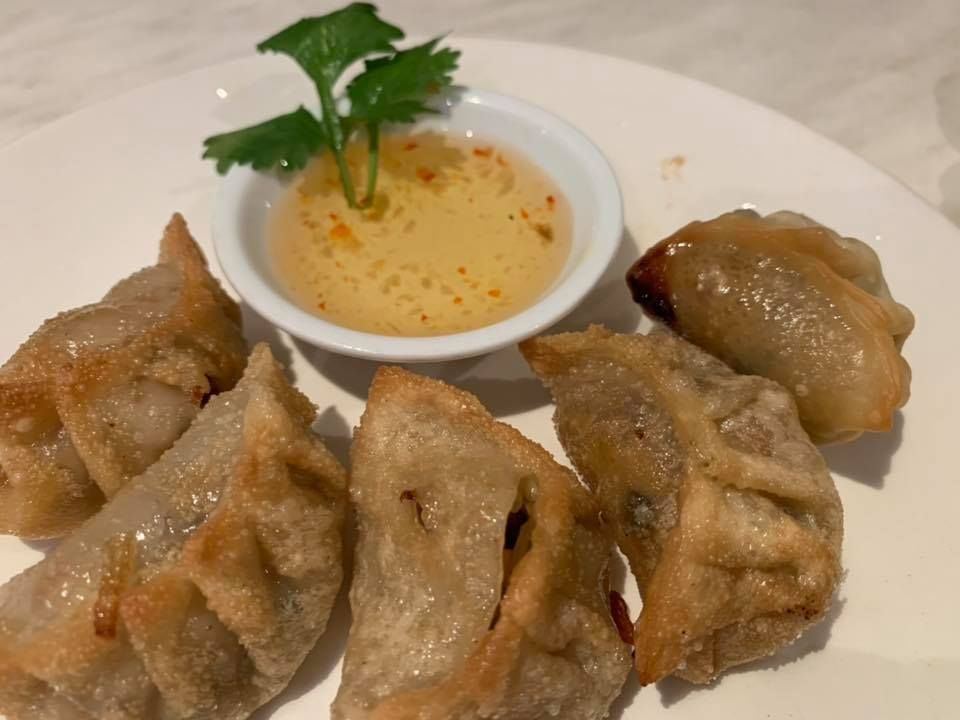 A white plate topped with fried dumplings and a small bowl of dipping sauce.