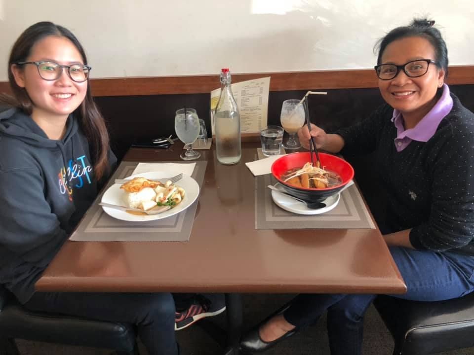 Two women are sitting at a table with plates of food and drinks.