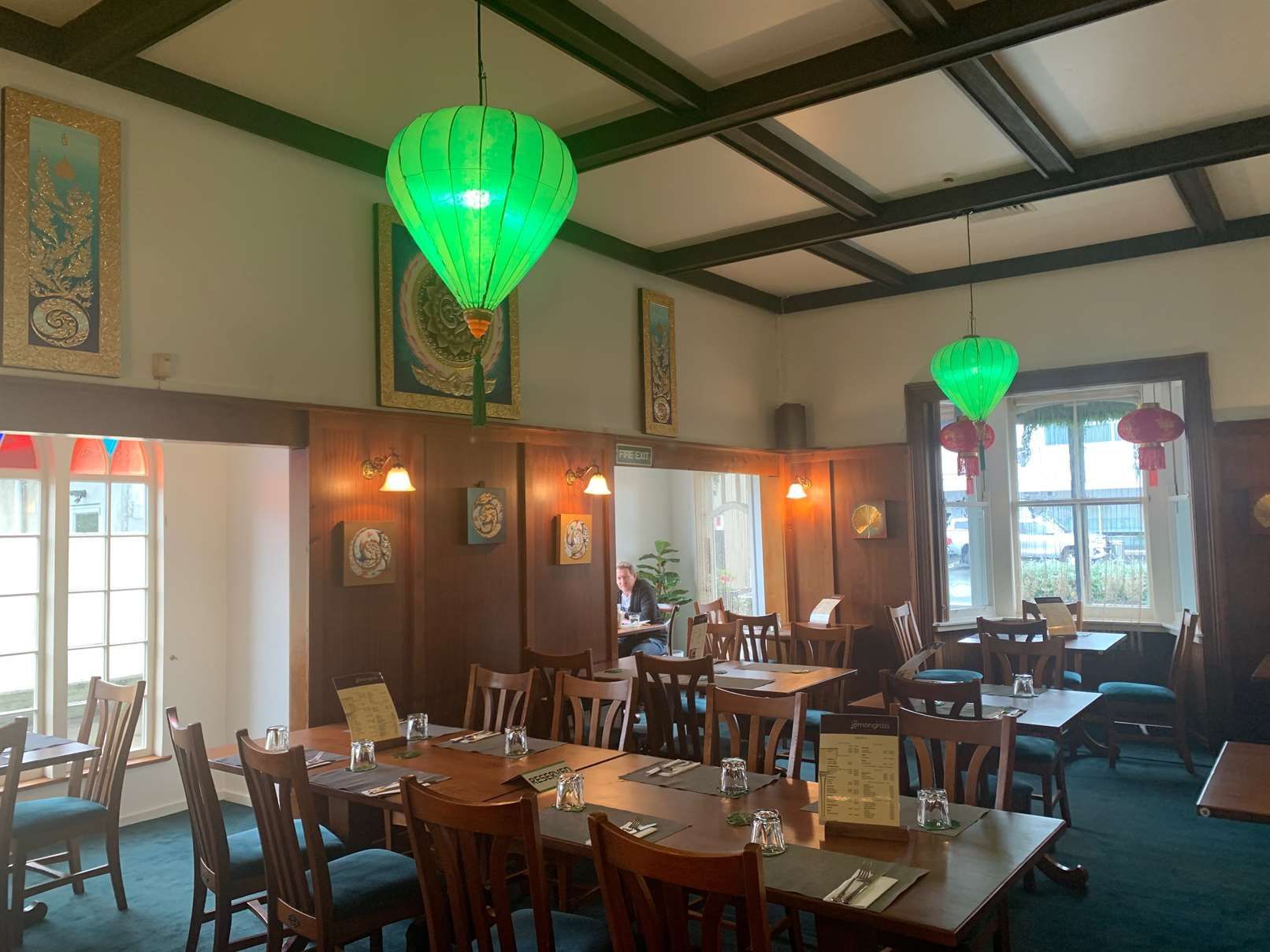 A restaurant with tables and chairs and green lanterns hanging from the ceiling.