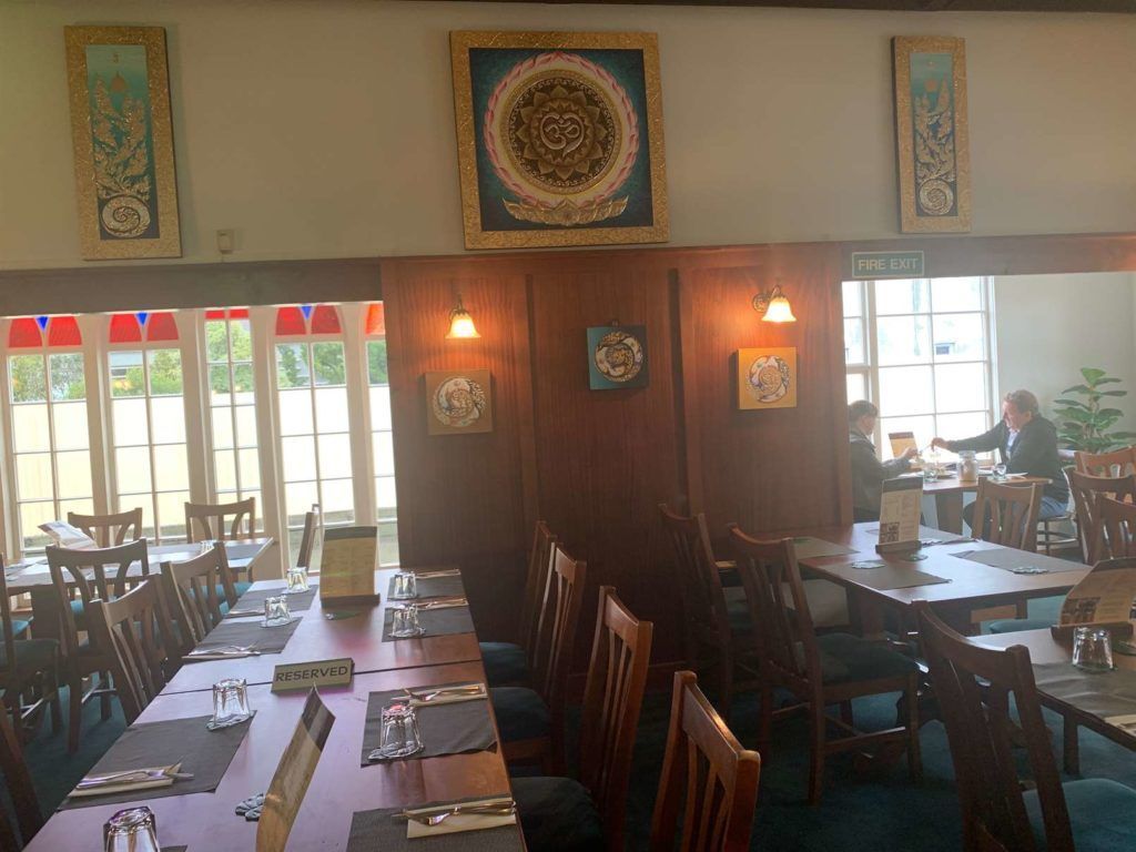 A restaurant with tables and chairs and a woman sitting at a table.