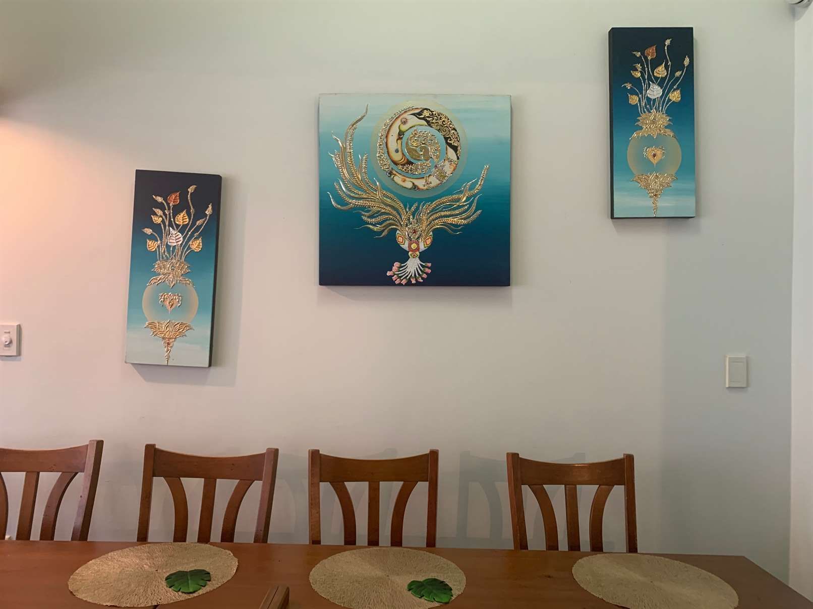 A dining room with a table and chairs and three paintings on the wall.