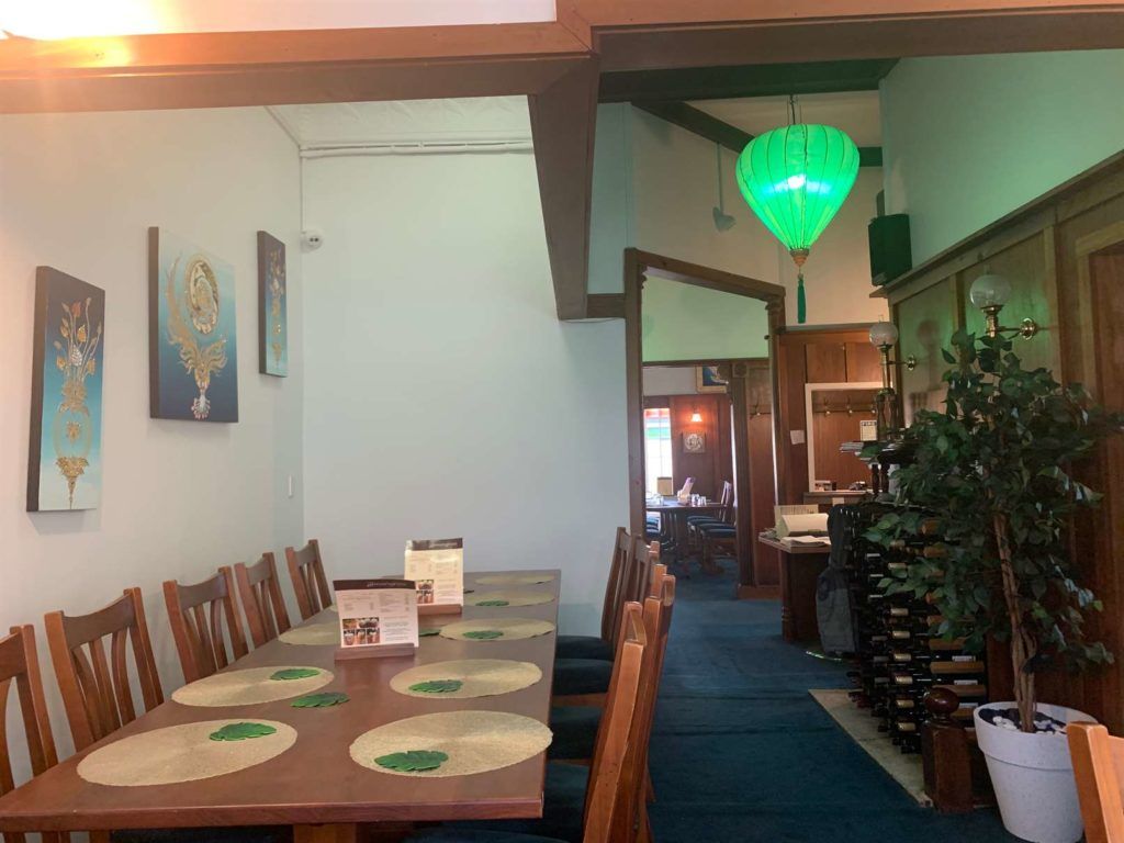 A long table and chairs in a restaurant with a green light hanging from the ceiling.