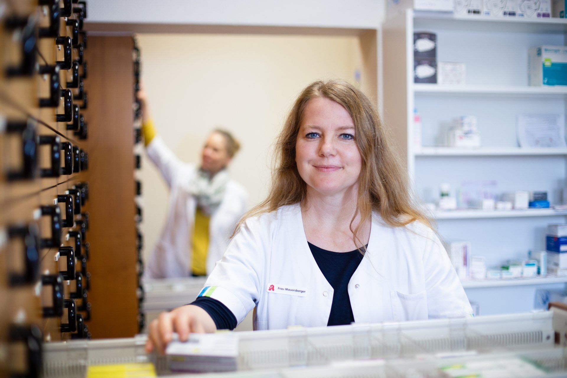 Eine Frau im weißen Kittel steht in einer Apotheke.