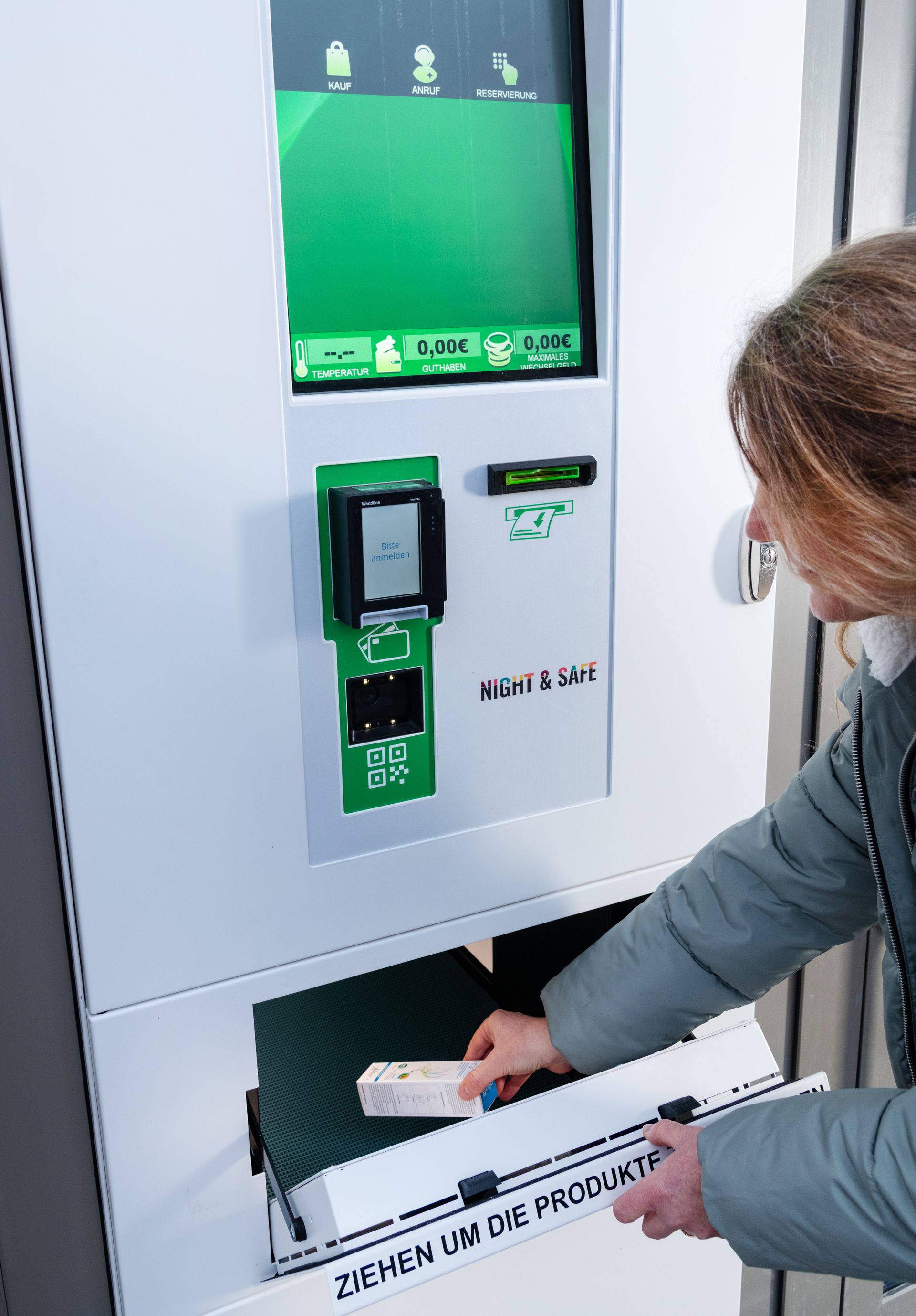 Eine Frau wirft ein Päckchen in einen weißen Recyclingautomaten mit grünem Display.