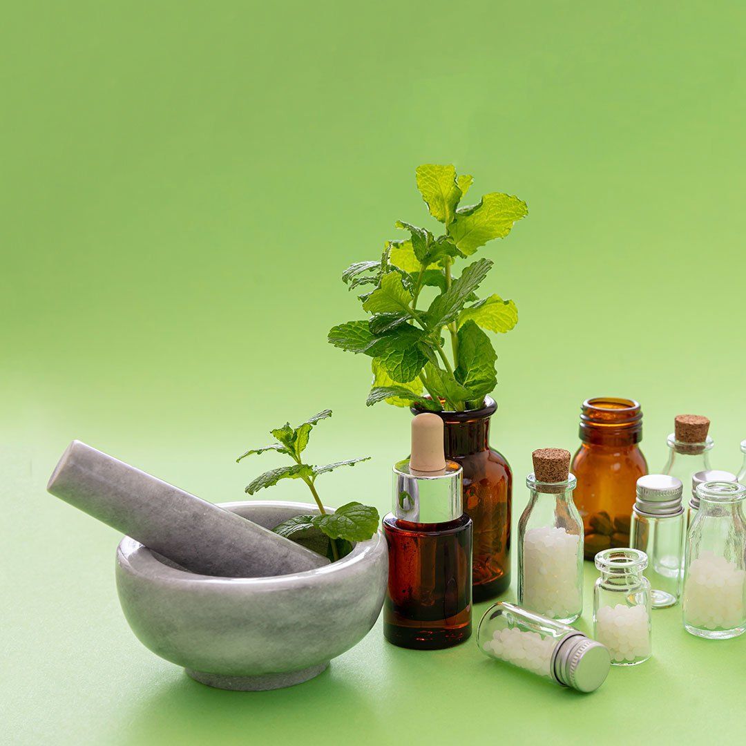 Mörser und Stößel mit Kräutern und Medikamentenflaschen vor grünem Hintergrund.