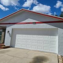 White garage door with red trim on a house under a blue sky.