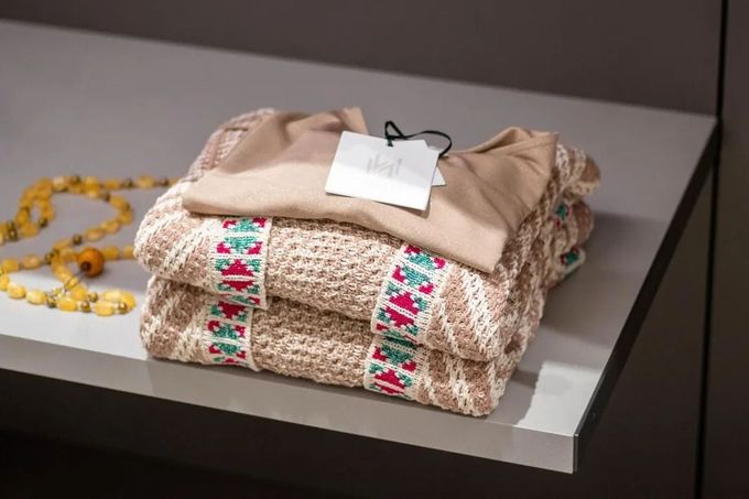 Maglioni color cuoio sovrapposti con una striscia decorativa ricamata e un'etichetta.