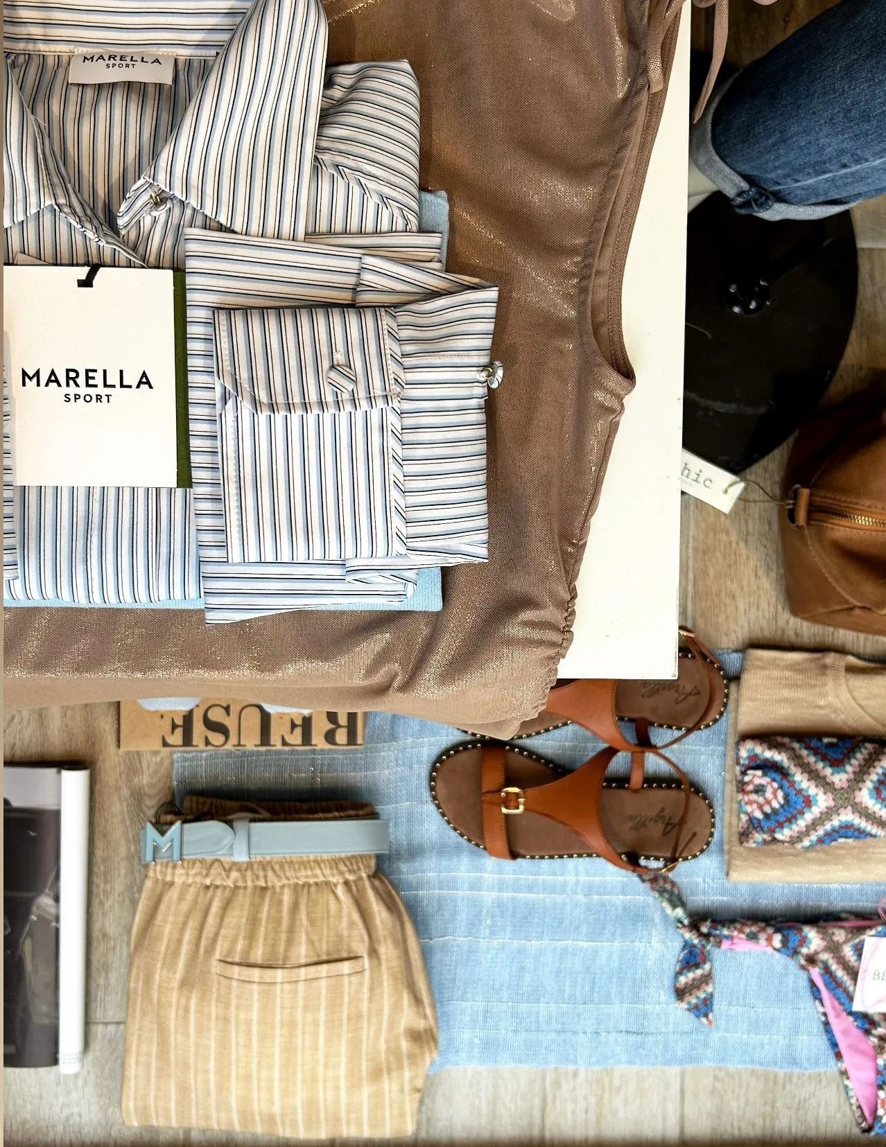 Abiti e accessori esposti: camicie a righe, pantaloni, sandali, borsa e un vestito con paillettes.