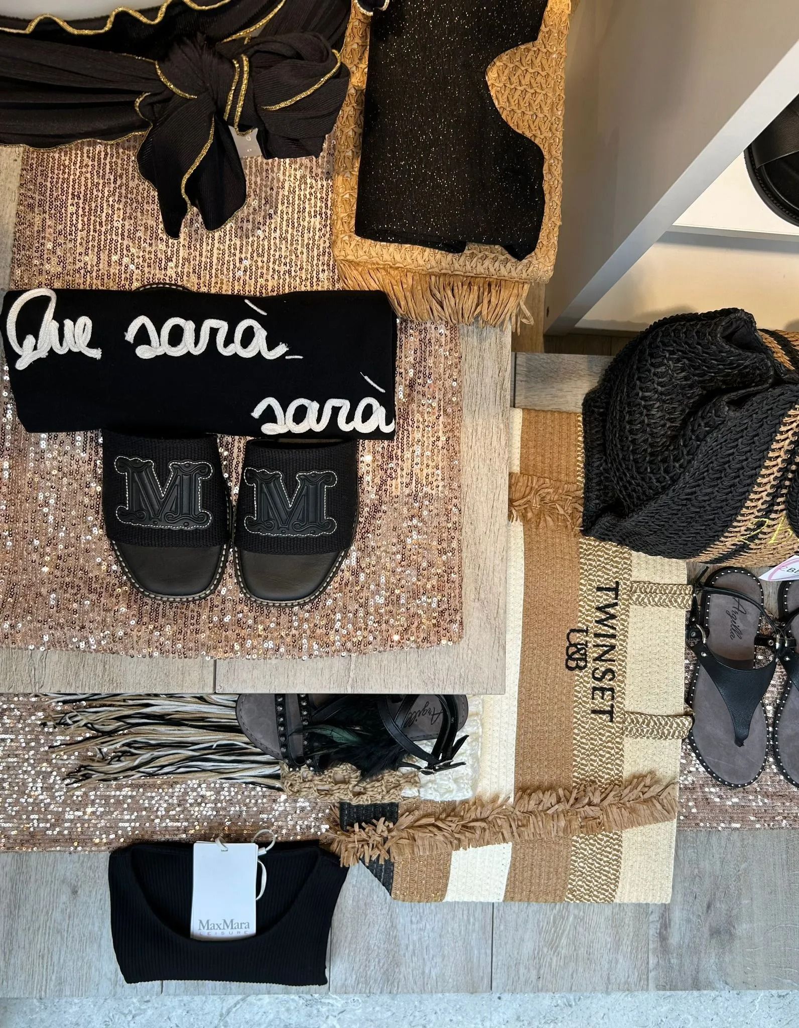 Esposizione di abiti, scarpe e accessori neri su superfici strutturate, tra cui una fascia nera con la scritta