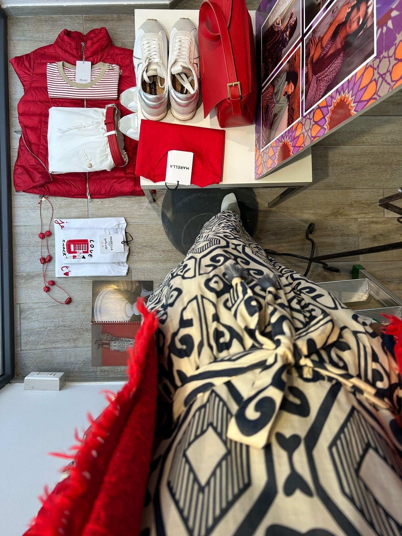 Esposizione di abiti: giacca rossa, borsa, scarpe, abito fantasia, articoli da regalo.