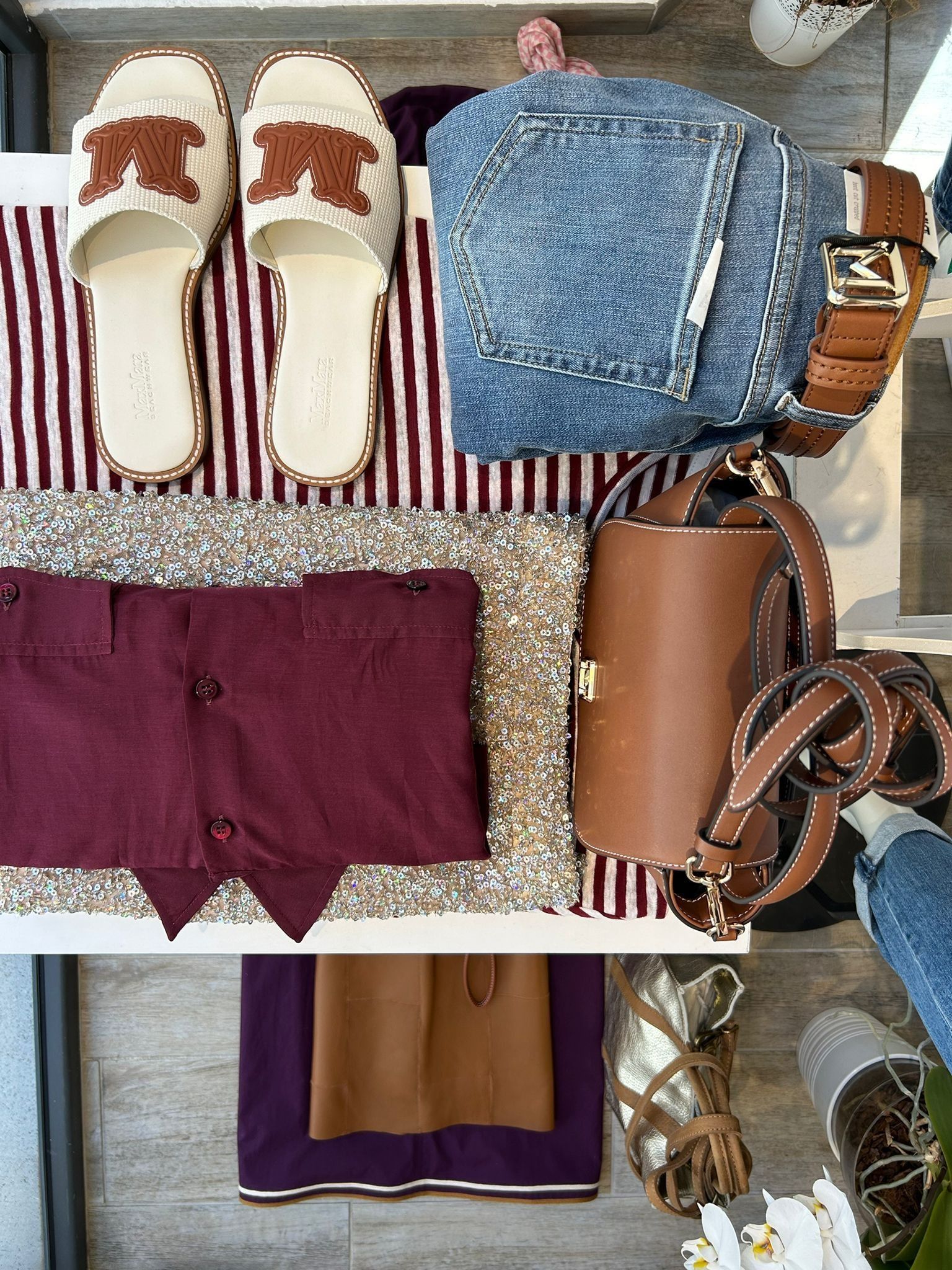 Flat lay di moda: jeans, top bordeaux, sandali, borsa marrone e cintura su sfondo a righe.