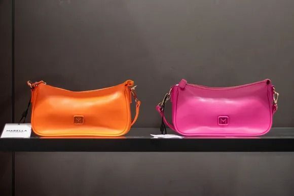 Due borse in pelle dai colori vivaci, una arancione e una rosa, esposte su uno scaffale.