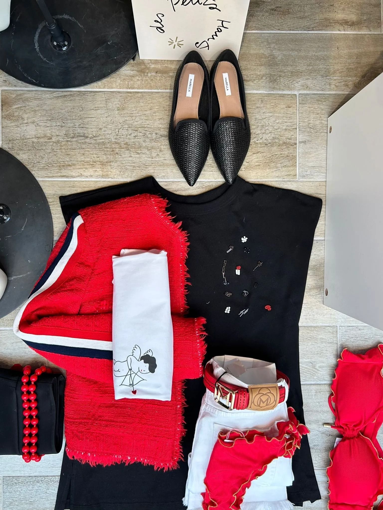 Disposizione piatta dell'outfit: scarpe nere, giacca rossa, camicia nera, gonna rossa, accessori rossi e asciugamano bianco su legno.