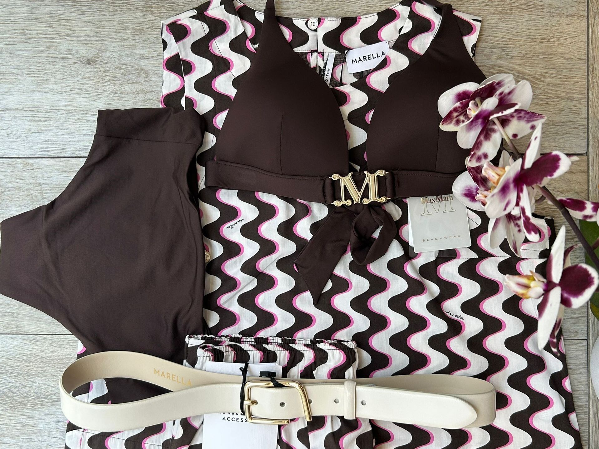 Completo composto da costume da bagno e bikini marrone, top e pantaloni a fantasia e cintura bianca; accanto a un'orchidea viola.