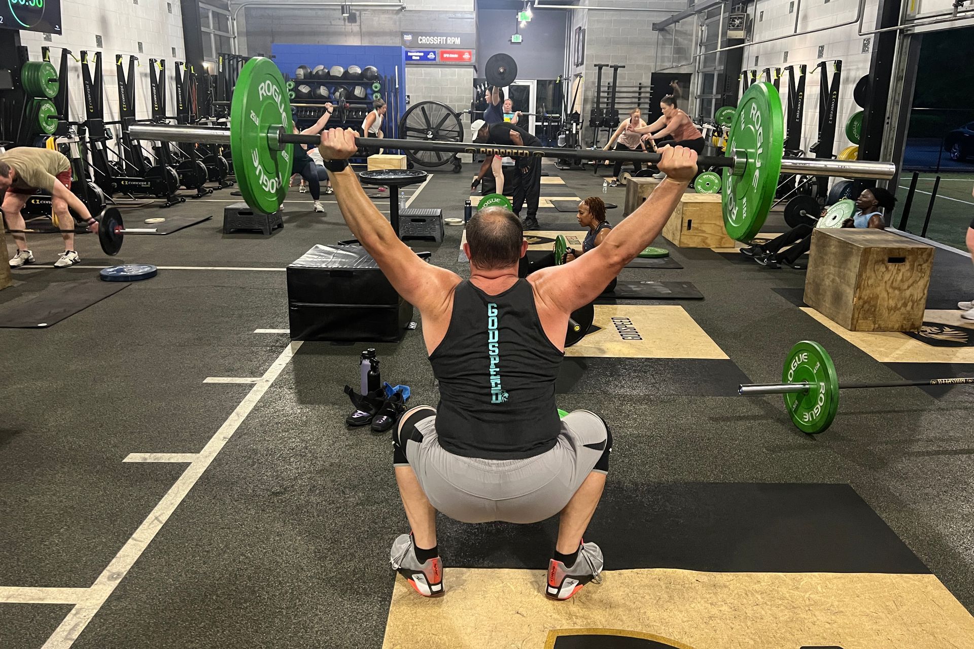 A man is squatting with a barbell over his head in a gym.