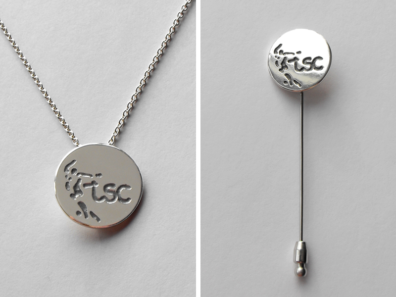 Zilveren sieraad met logo van voetbalclub. Te dragen als speldje of aan een ketting.