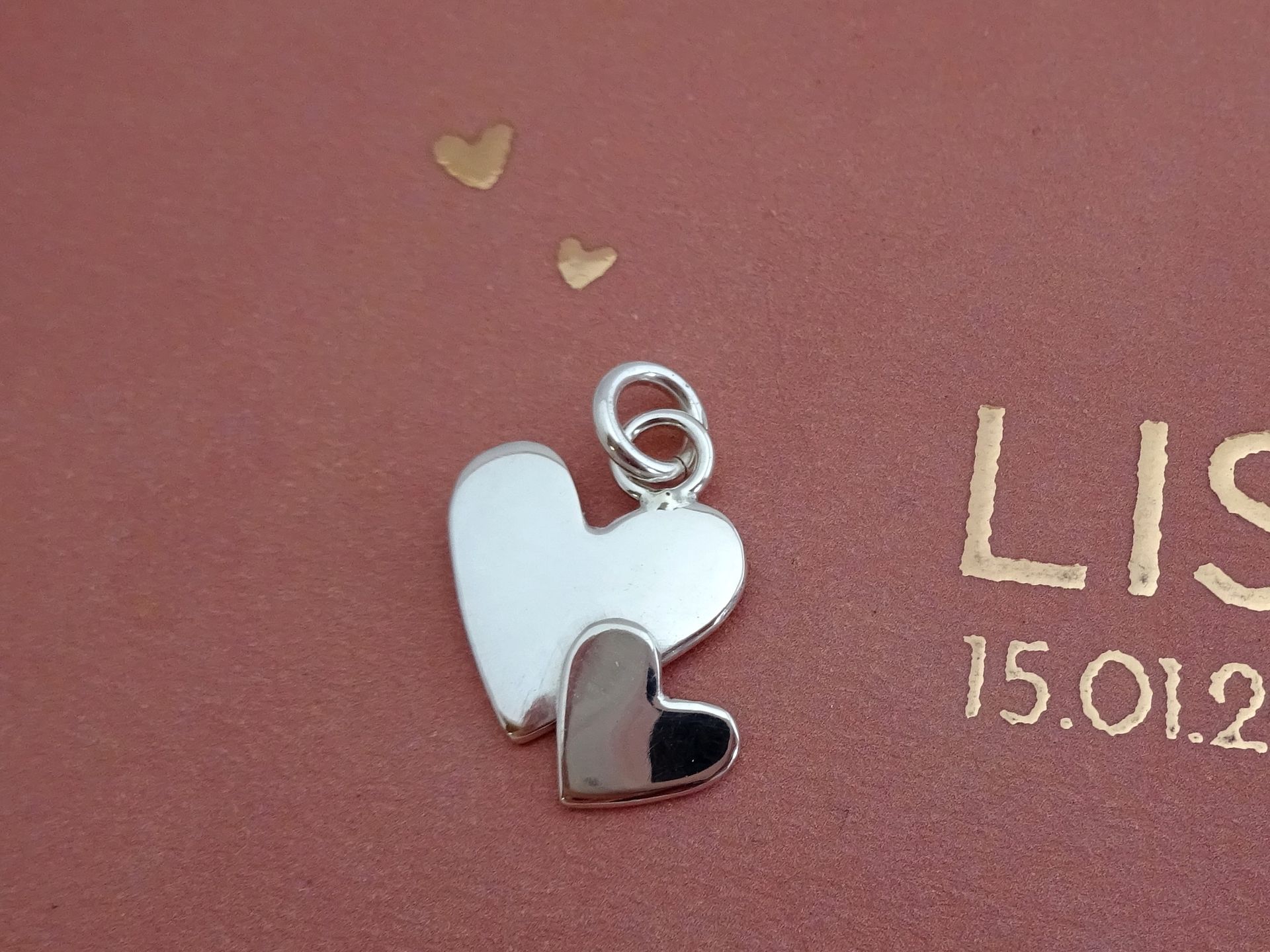 Bedeltje van zilver met hartjes. Dezelfde als van het geboortekaartje.