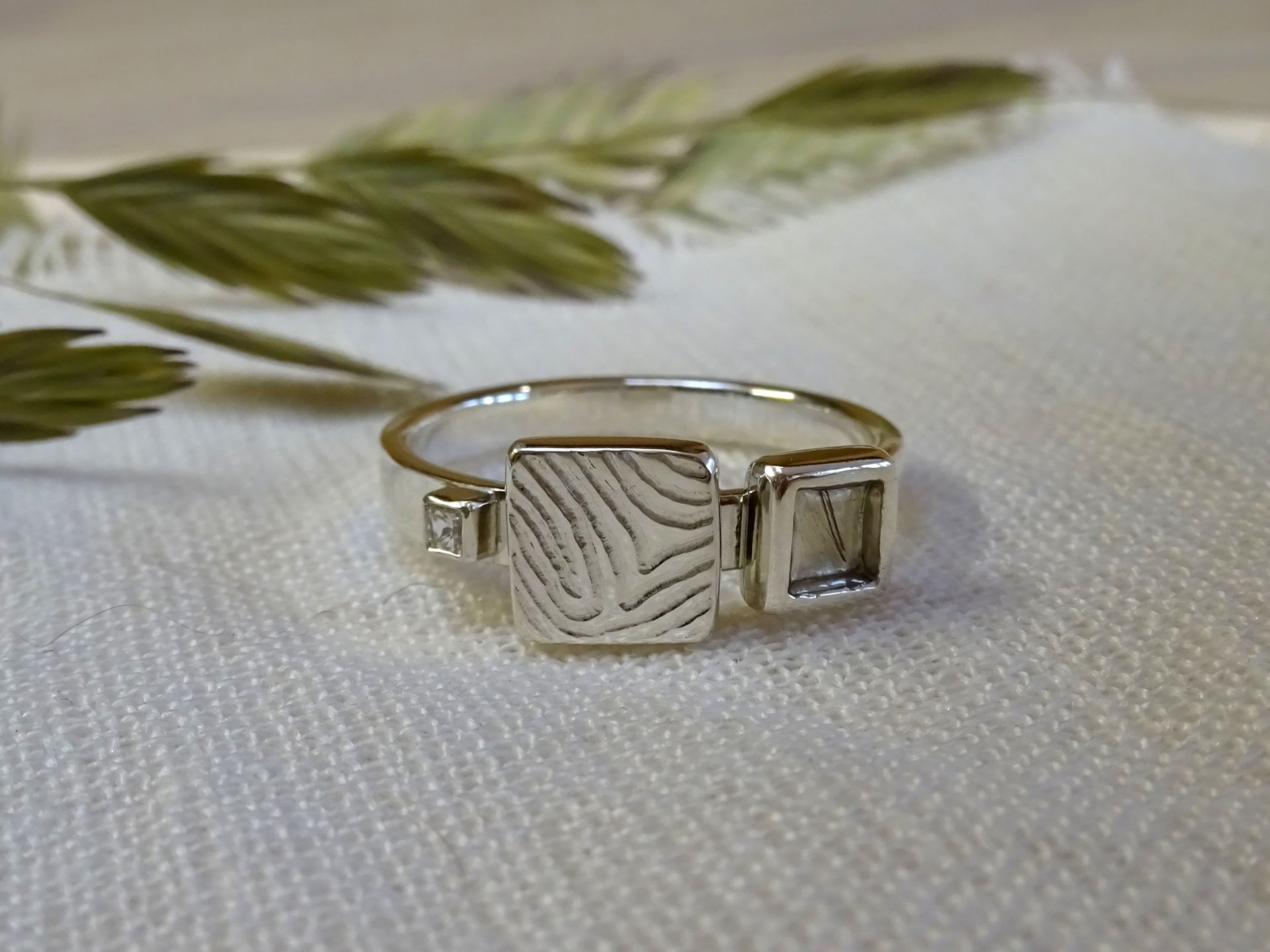 Ring van zilver met een vingerafdruk, een plukje haar en een vierkante zirconia.