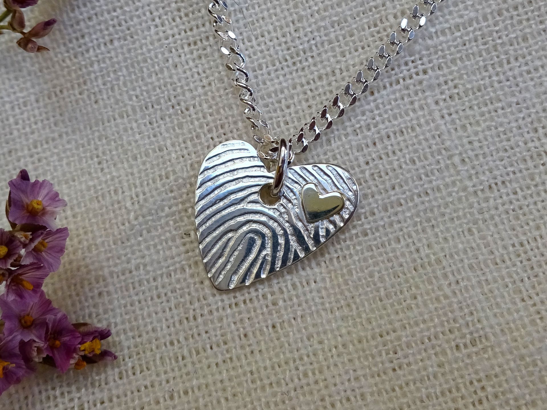 Zilveren bedeltje van een hartje met en klein gouden hartje en een vingerafdruk.