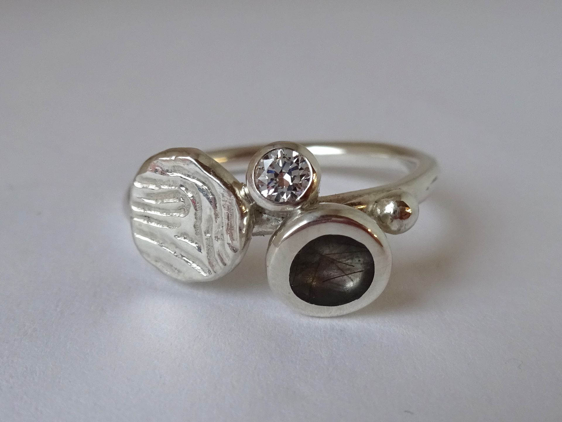 Zilveren ring met vingerafdruk, plukje haar van de overledene, bolletje zilver en zirconia.