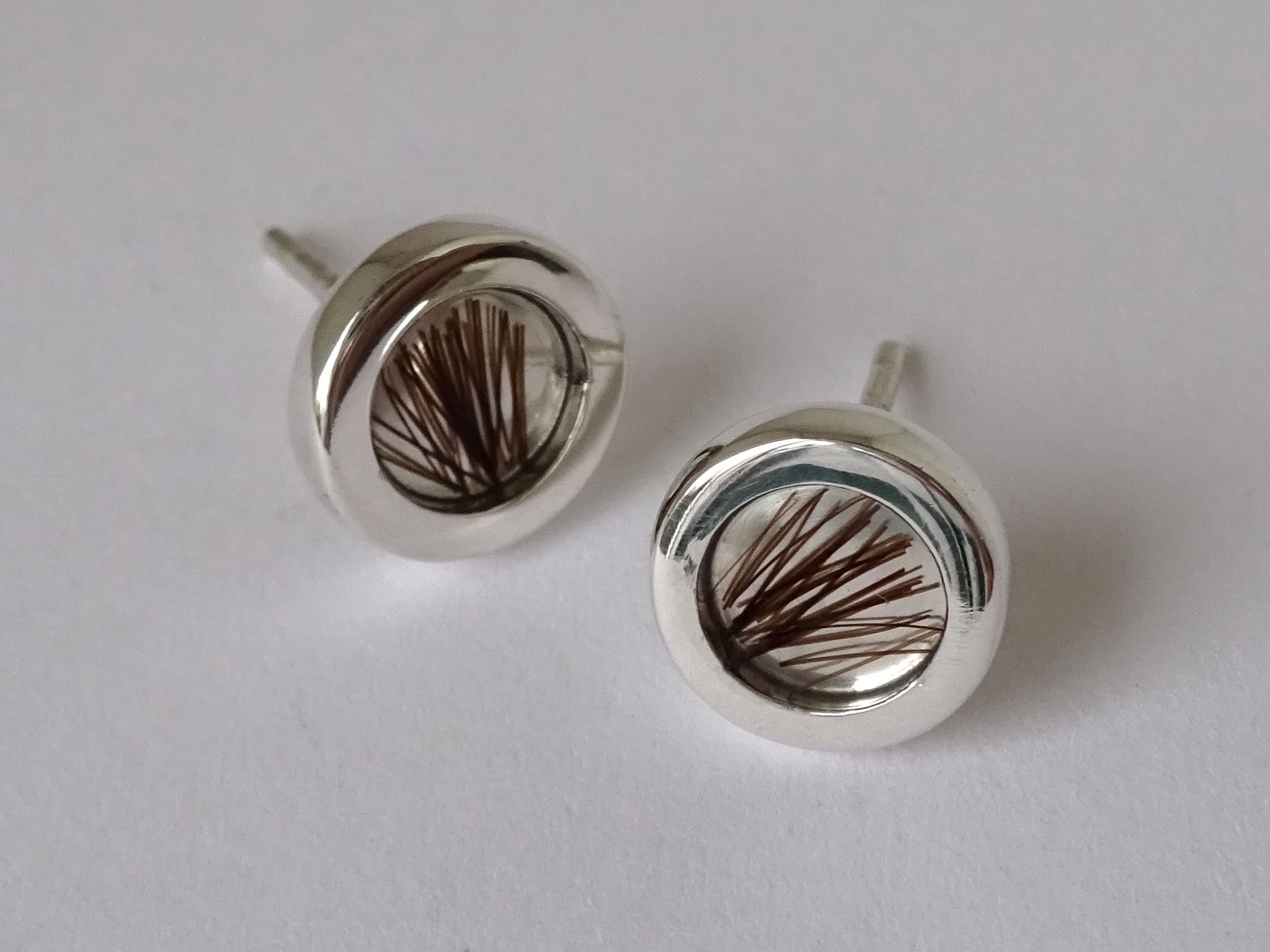 Oorknopjes van zilver met een plukje haar in hard gegoten.