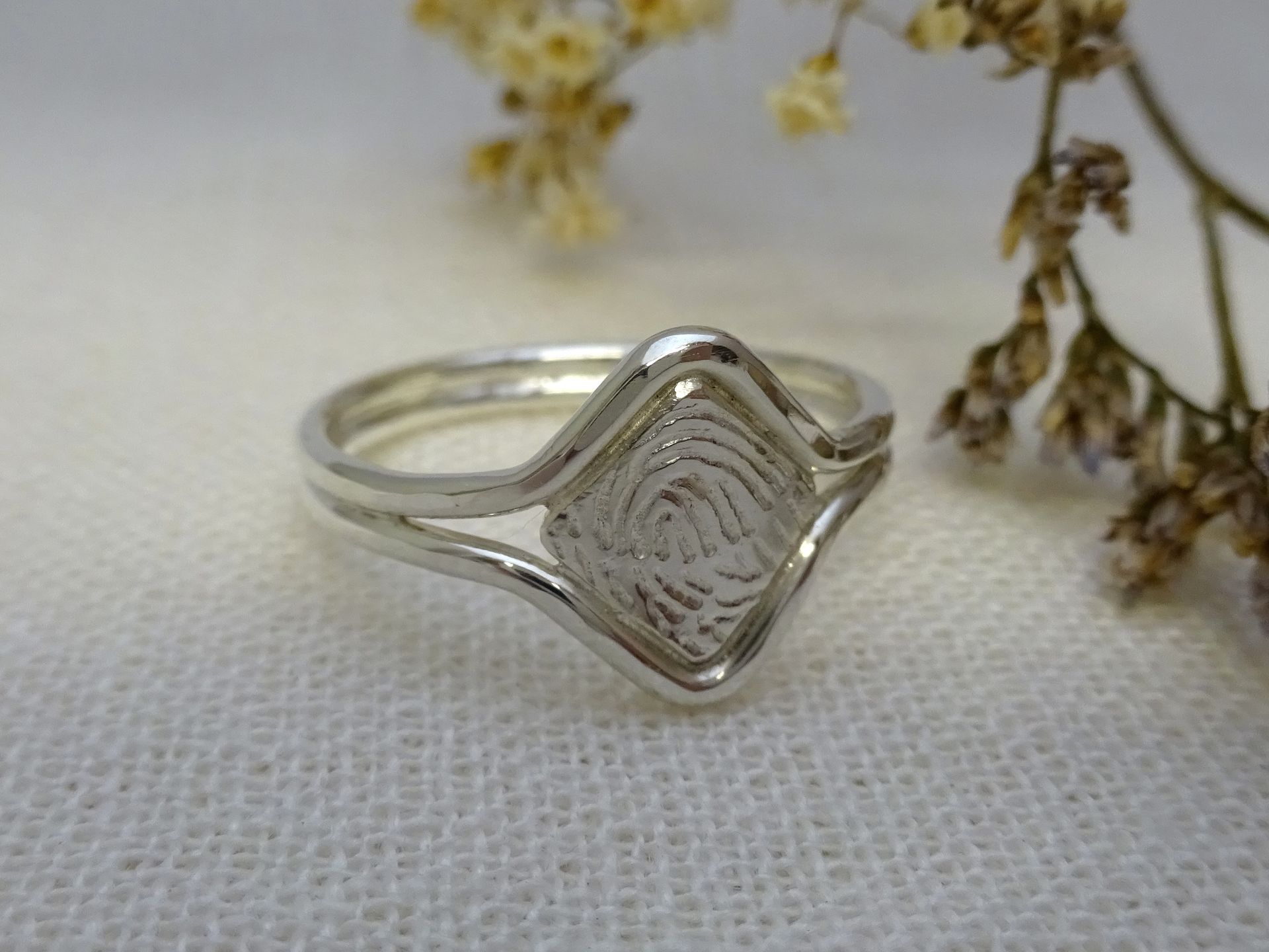Zilveren ring met vingerafdruk op vierkant plaatje, omsloten door 2 ronde draden.