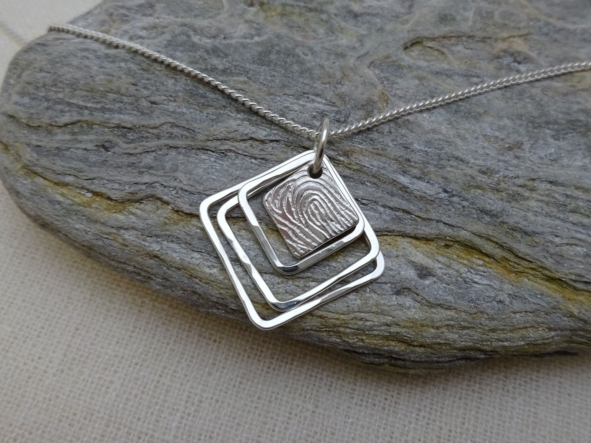 Hanger van zilver met losse open vierkanten en een plaatje met vingerafdruk.