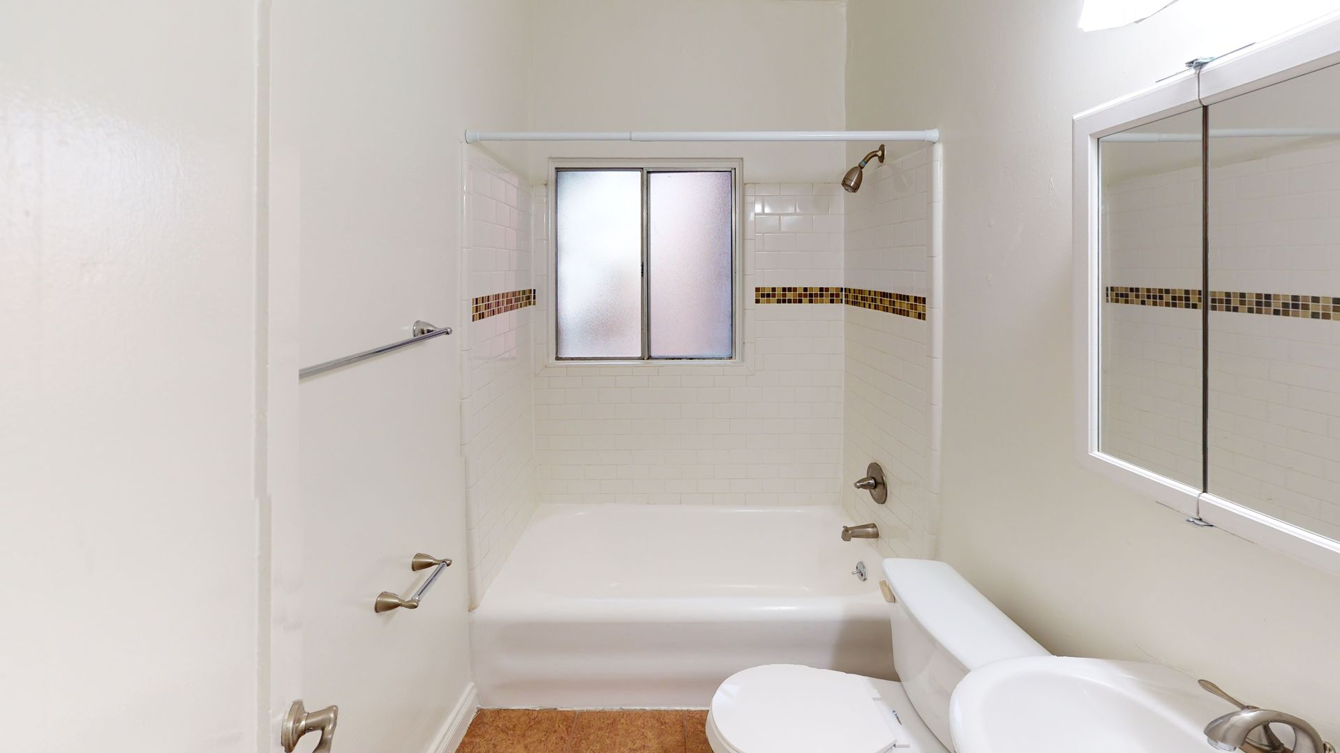 Bathroom with a white tub and toilet, a window, and a mirror.