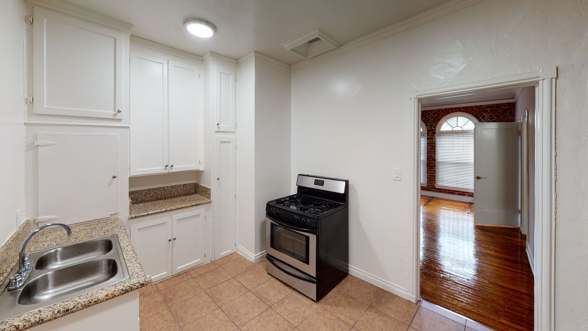 Kitchen with white cabinets, stainless steel oven, and a doorway to another room.