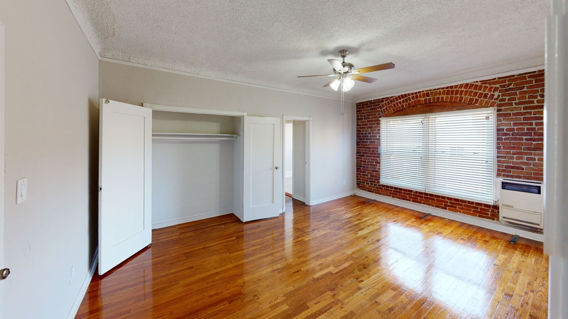 Bedroom with hardwood floors, exposed brick accent wall, white closet doors, and ceiling fan.