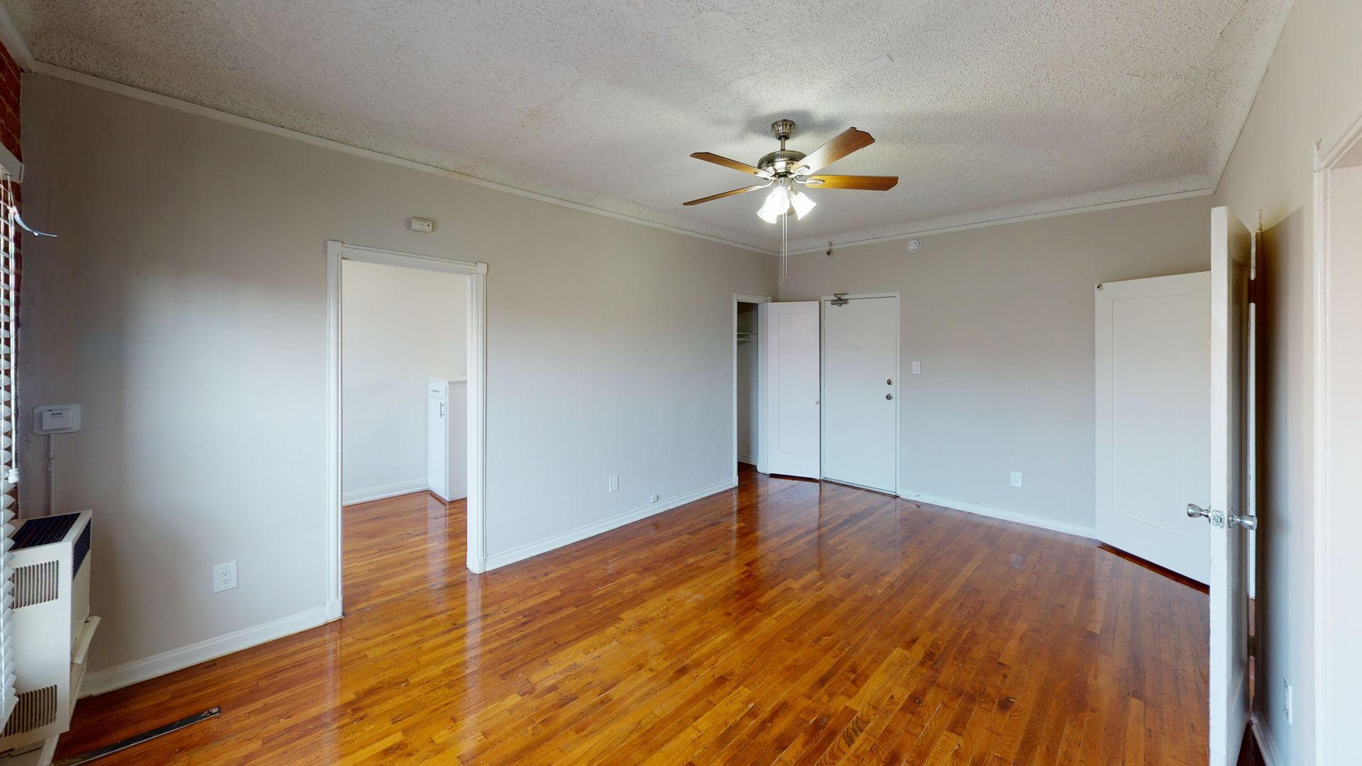 Wooden-floored room with gray walls, white trim, and a ceiling fan. Two doorways and an open door are visible.