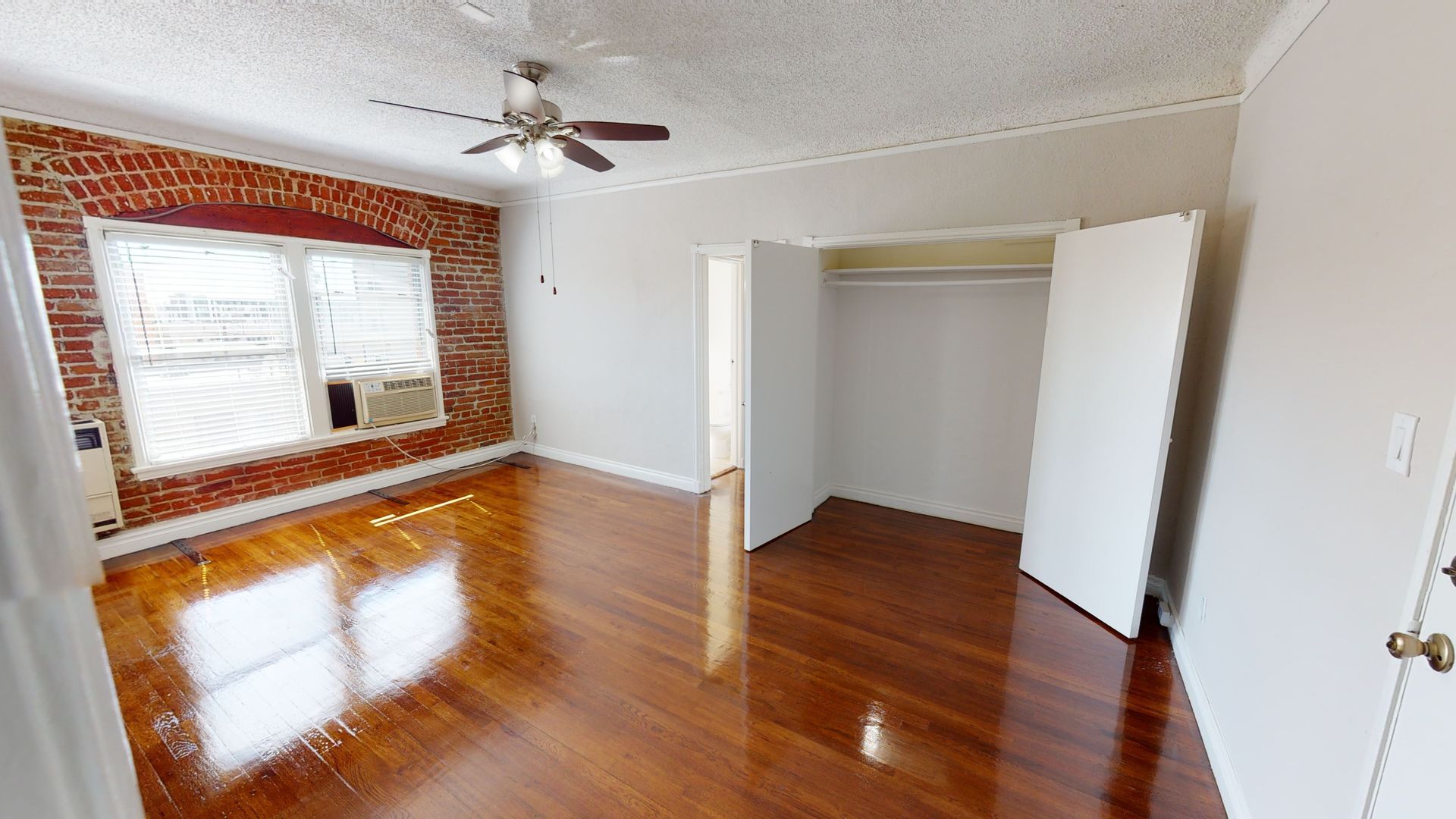 Bedroom with exposed brick wall, hardwood floors, closet, and window.