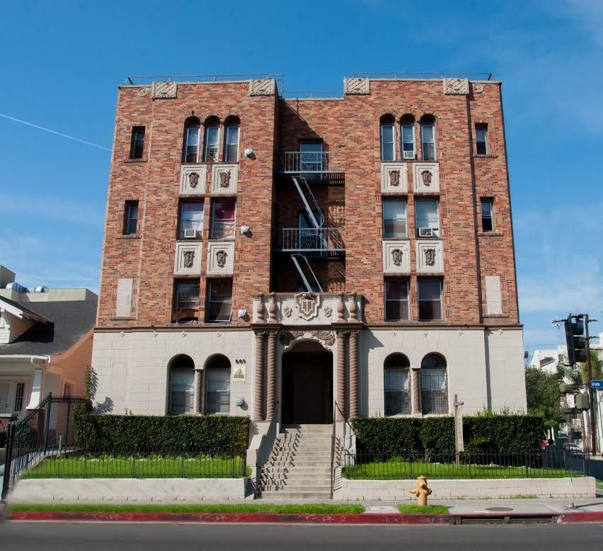 Multi-story brick apartment building with white accents, fire escape, and front steps.