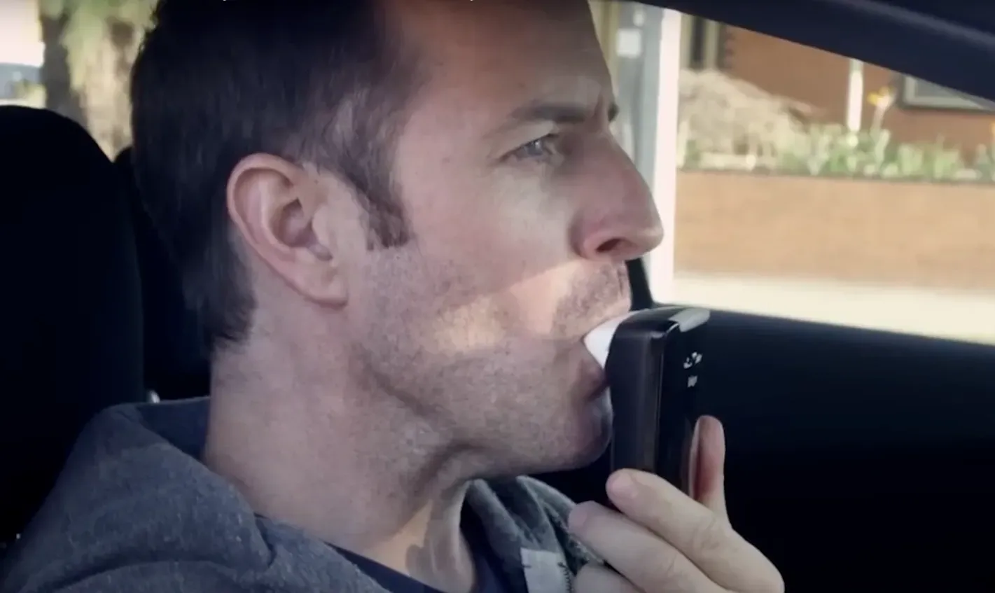 Man in car blowing into a breathalyzer device. — All Coast Auto Solutions in Noosaville, QLD