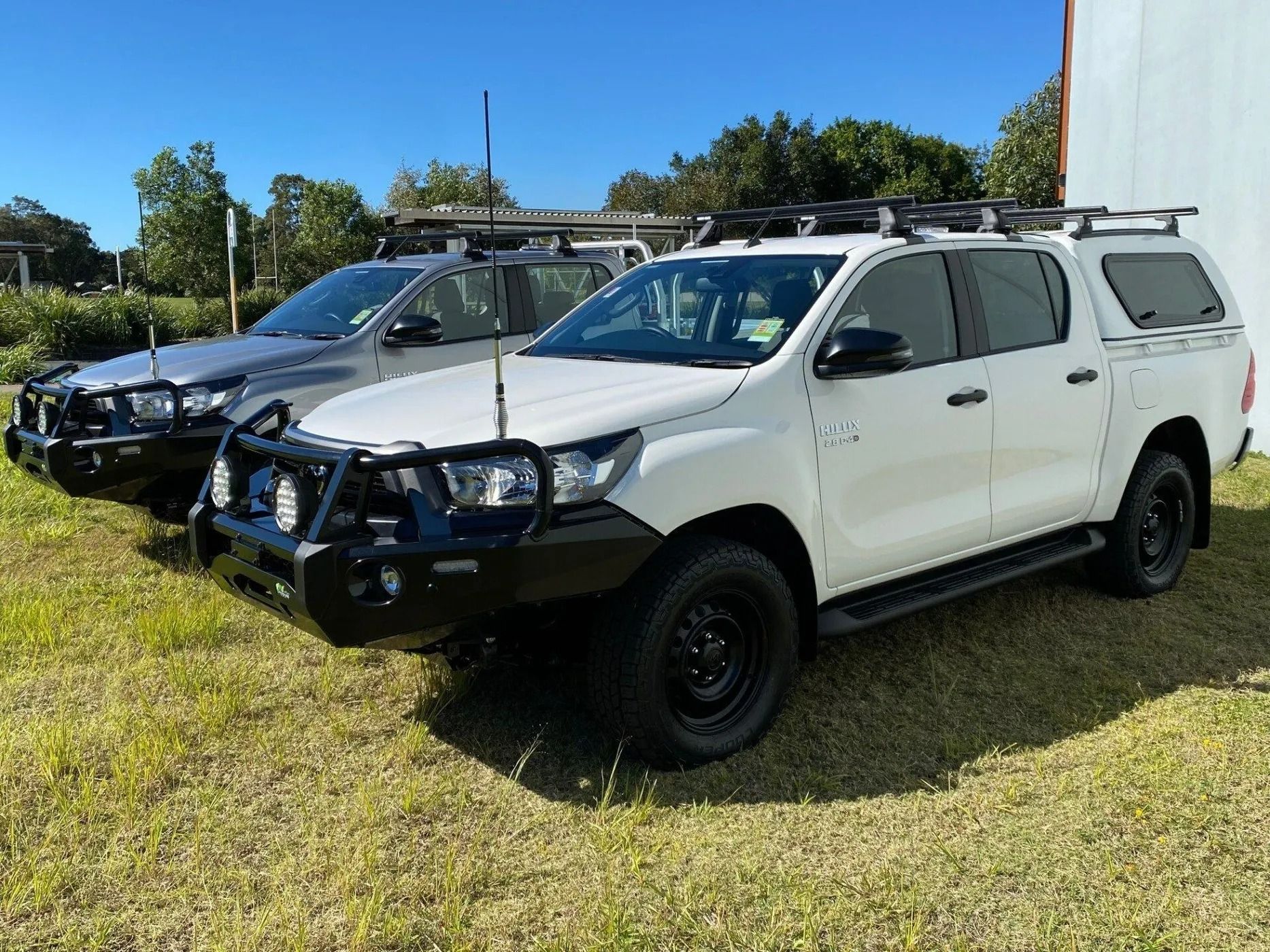 Two Toyota Hilux Trucks One Gray and One White Parked on Grass — All Coast Auto Solutions in Noosaville, QLD