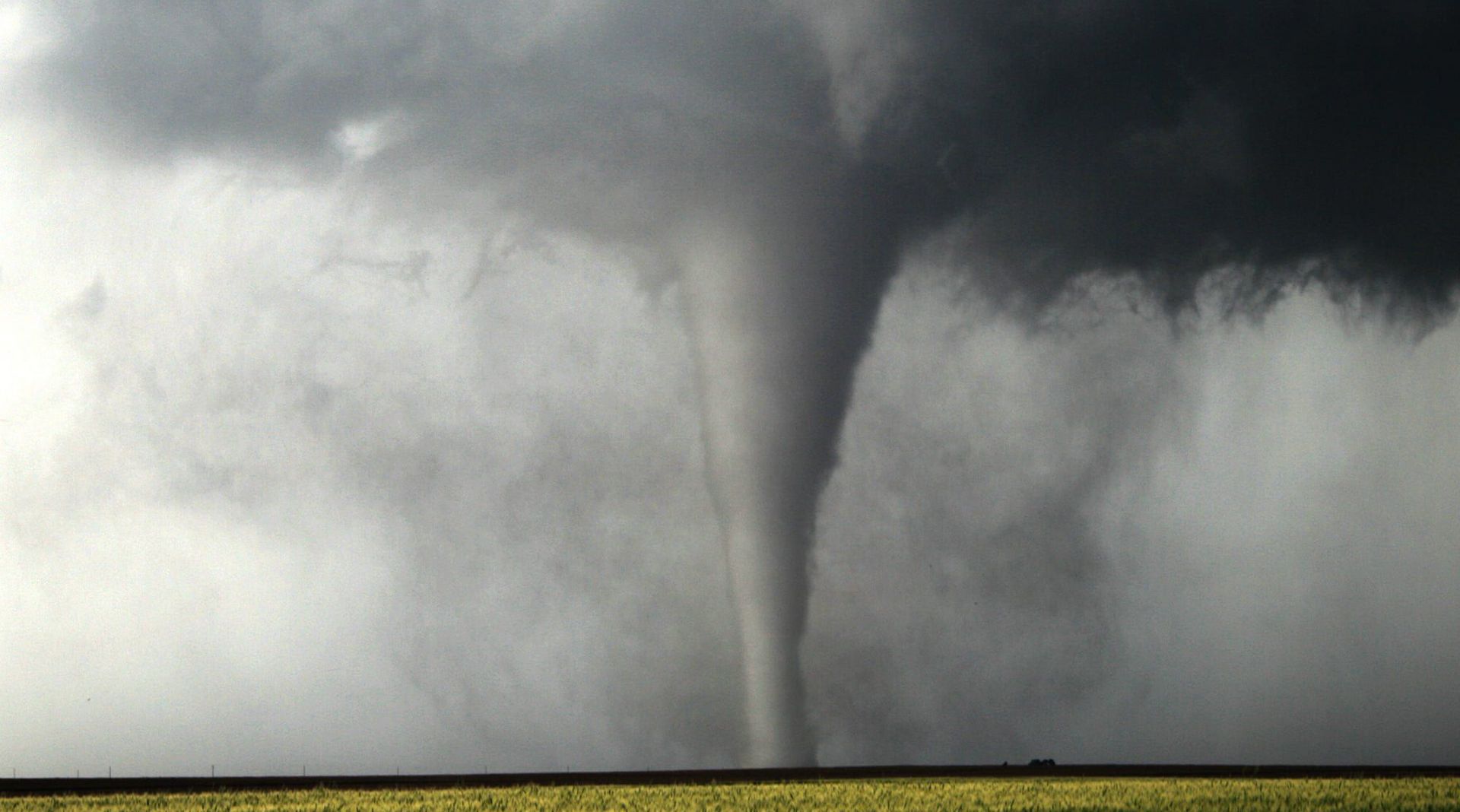 A tornado is moving through a field on a cloudy day.