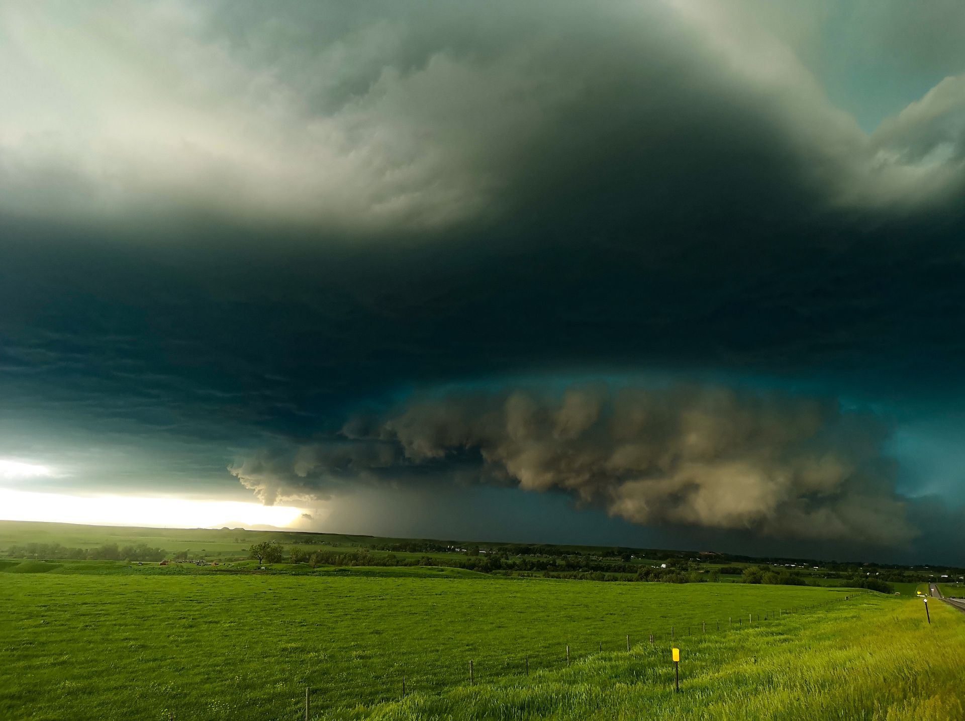 A large storm cloud is moving over a green field.