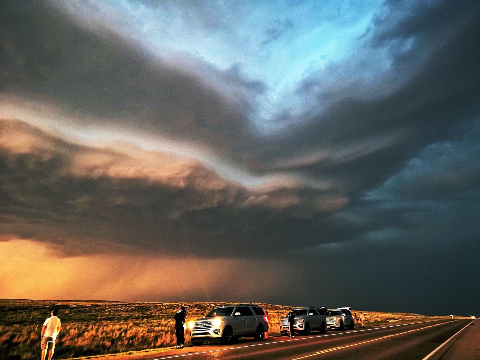 A group of people standing on the side of a highway watching a storm