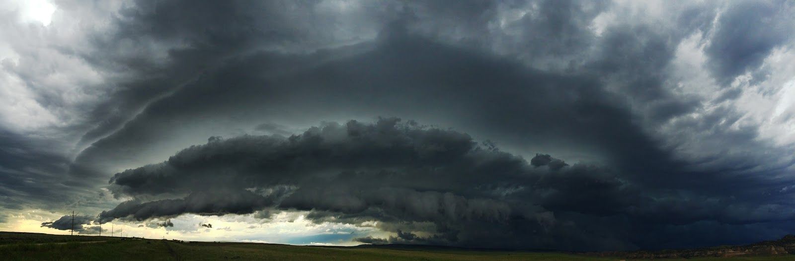 A large storm cloud is moving over a field.