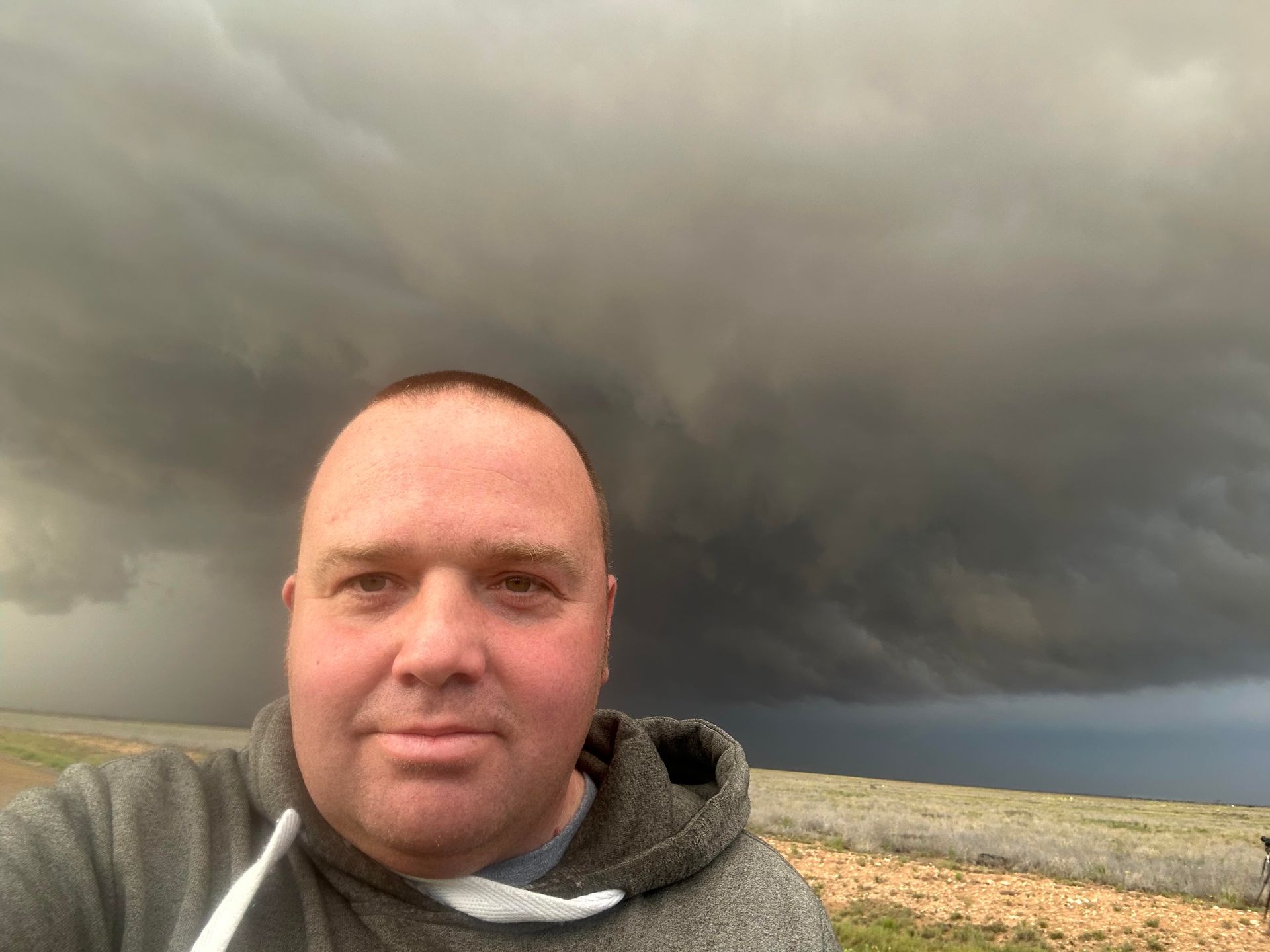 A man is taking a selfie in front of a cloudy sky.