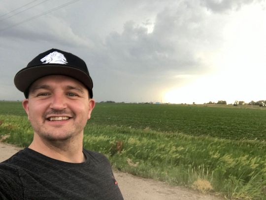 A man wearing a hat is standing in front of a field.