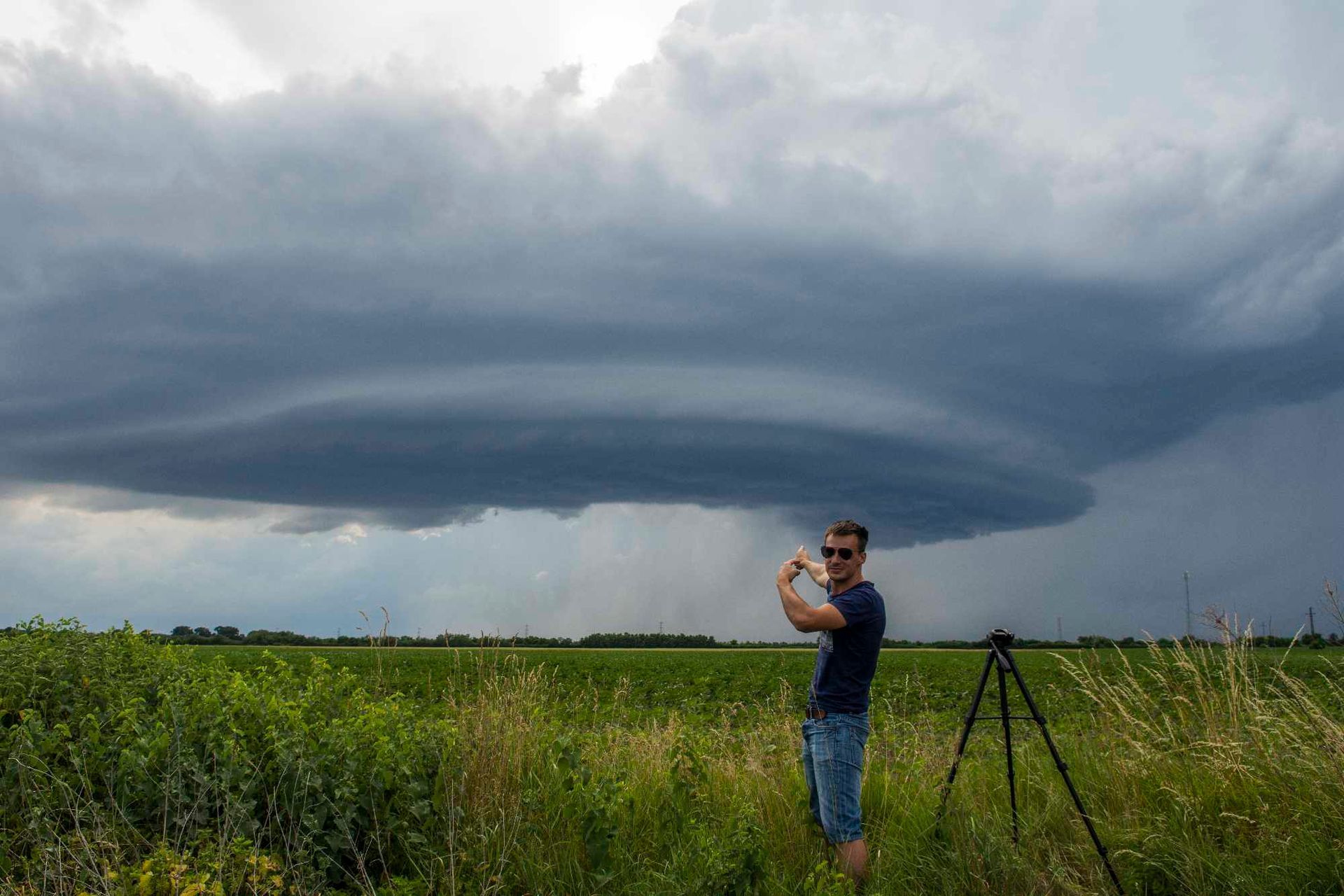 A man is standing in a field taking a picture of a tornado.