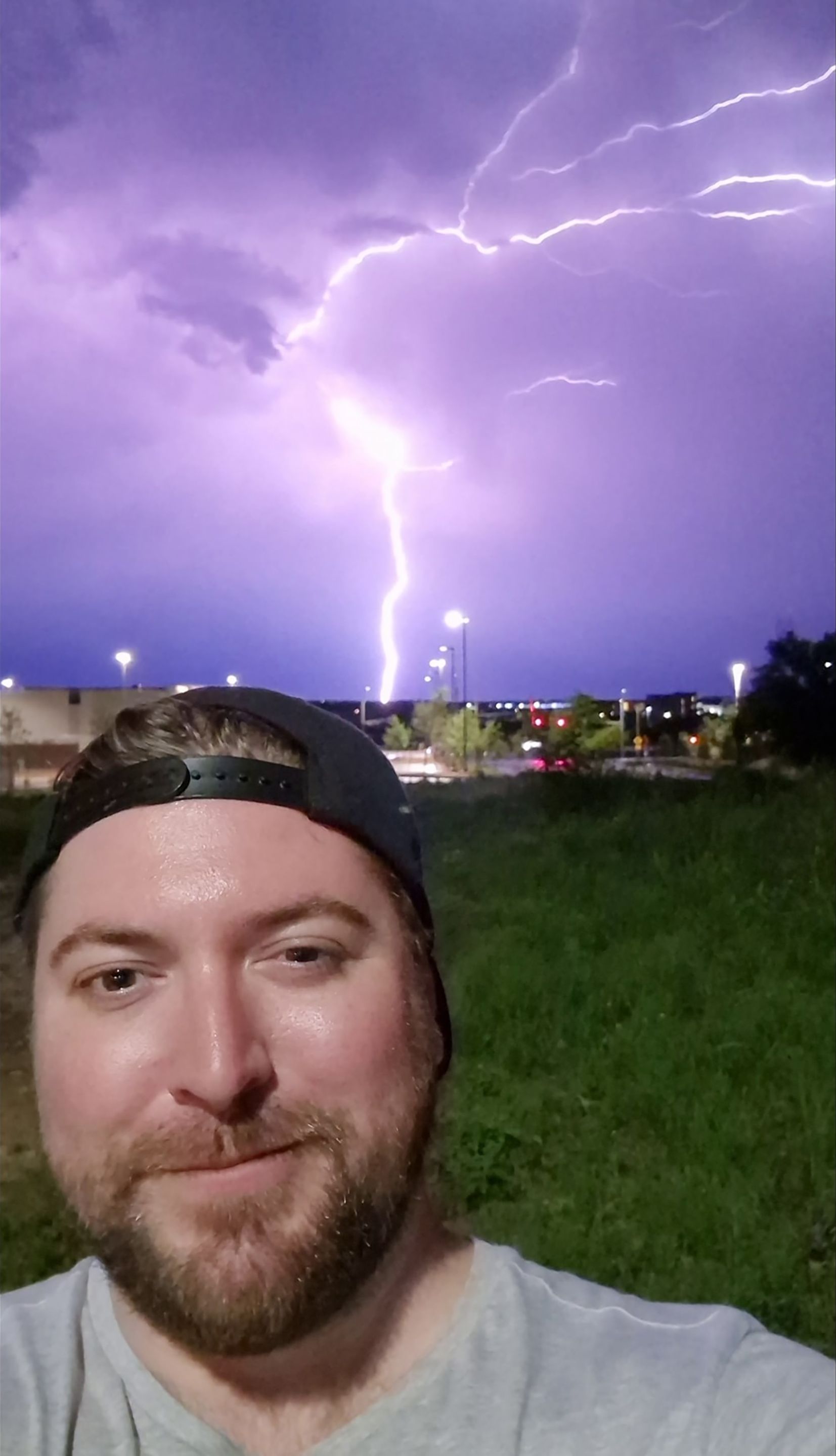 A man is taking a selfie in front of a lightning storm.