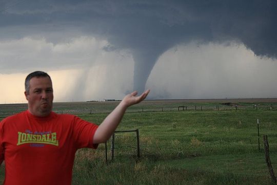 A man in a red lonsdale shirt is standing in front of a tornado.