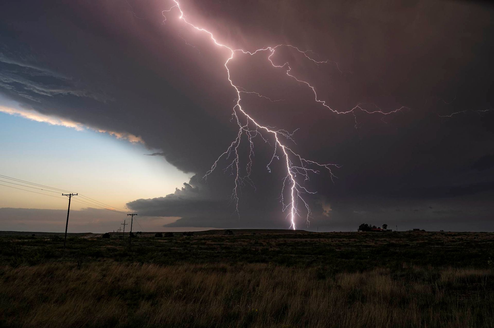 A lightning bolt is strikes in the sky over a field.