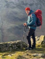 A man with a backpack and walking poles is standing on top of a mountain.