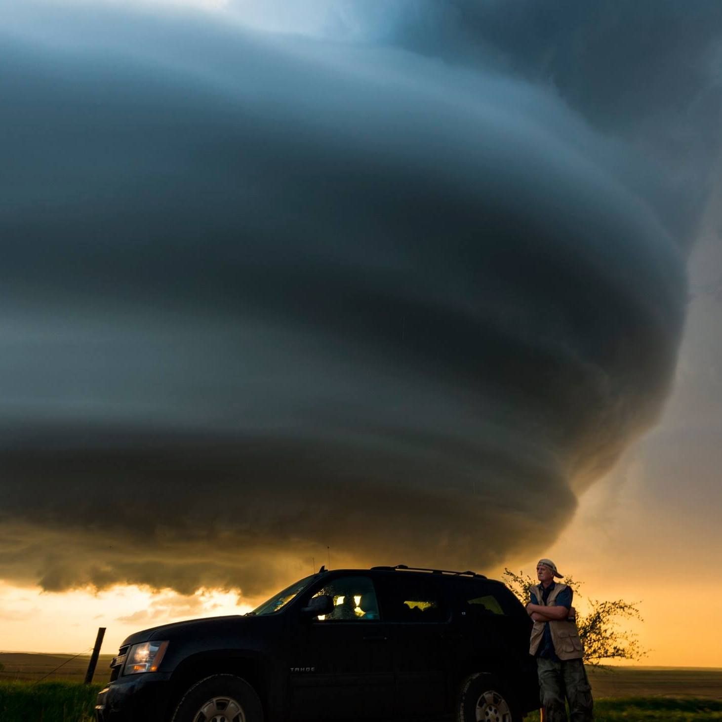 A man is standing next to a car in front of a large storm cloud