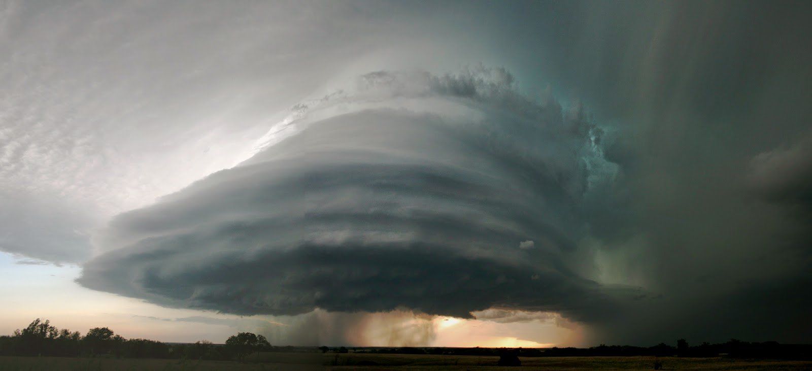 A large tornado is moving through a field with lightning.