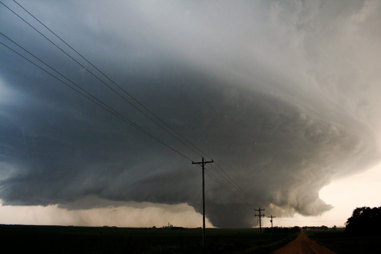 A large tornado is moving through a field with power lines in the foreground.